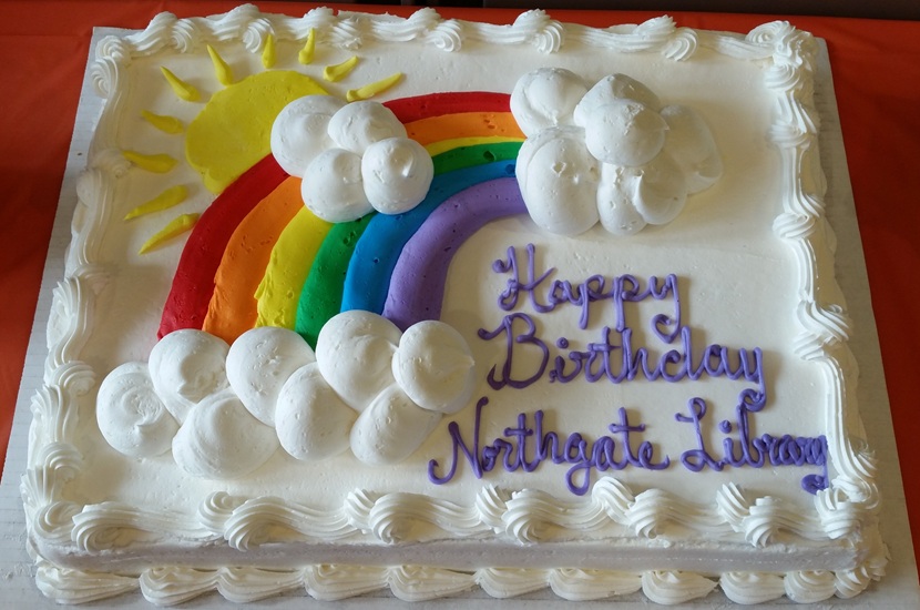Photo of a white rectangular cake with frosting that says "Happy birthday, Northgate Library," with a rainbow, a sun, and clouds