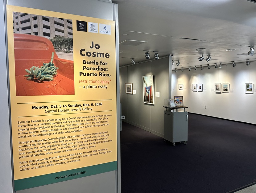 A photograph of an art gallery at the Central Library, showing a poster of an exhibit opening into a gallery showing a collection of photographs.